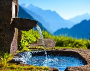 fontana in pietra fra le montagne con acqua limpida che sgorga